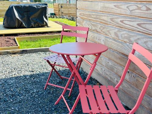 a red table and two chairs sitting next to a building at jolie chalet Normand - classée 3 étoiles in Beuzeville