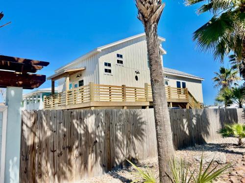 una casa sulla spiaggia con una recinzione e una palma di Famous Port A Pelican House Stunning NEW construction Walk to Marina & Bars a Port Aransas