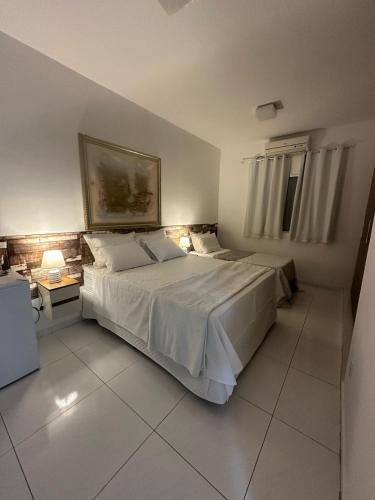 a bedroom with a white bed with a painting on the wall at Torquato Flats Orla in Petrolina
