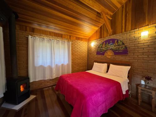 a bedroom with a bed with a red blanket and a fireplace at Chalés Das Estrelas in Visconde De Maua