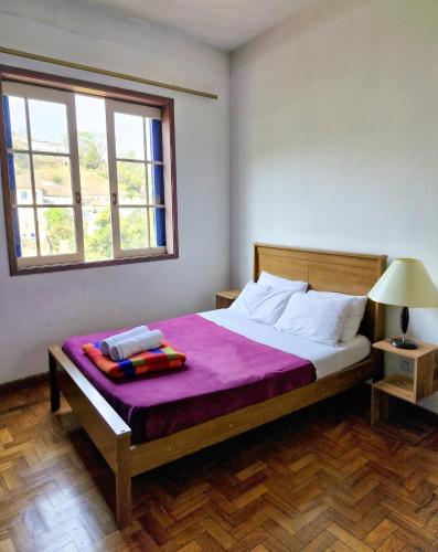 a bedroom with a bed with purple sheets and a window at Varanda Pouso e Arte in Ouro Preto