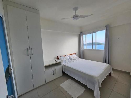 a white bedroom with a bed and a window at Apartamento frente ao mar de Angra in Mangaratiba