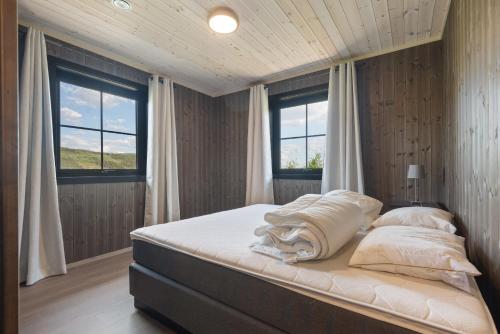 a bed in a bedroom with two windows at Trysil 豪华全新小木屋住宿 in Nybergsund
