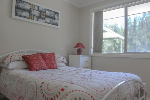 a bedroom with a bed with red pillows and a window at Central Hideaway at Black Head in Hallidays Point