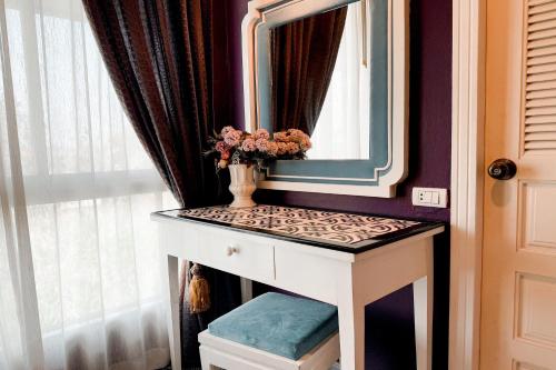 a dressing table with a mirror and a vase with flowers on it at Rasa Boutique Hotel Chiang Rai in Chiang Rai
