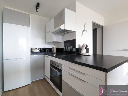 une cuisine avec des armoires blanches et un comptoir noir dans l'établissement Appartement rénové au pied de la plage avec balcon et parking - FR-1-825-46, à La Rochelle