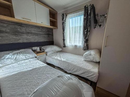 een slaapkamer met twee bedden en een raam bij Stunning Caravan With Decking At Haven Hopton-On-Sea Ref 80007L in Great Yarmouth