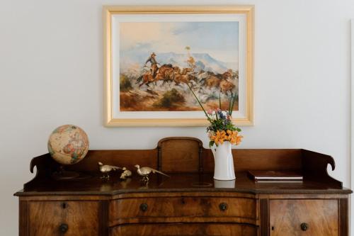 a painting on the wall above a desk with a vase of flowers at Domaine du Moine in Oakhampton