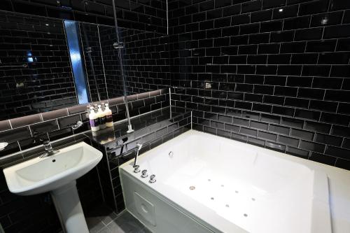 a black tiled bathroom with a tub and a sink at Hotel Kkuljam Stay in Jinju