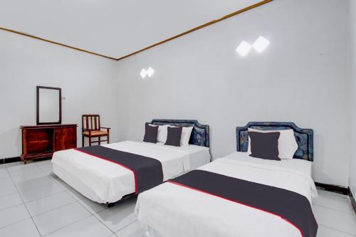 two beds in a room with a mirror and a chair at Hotel O Kaliurang Near Gunung Merapi Kaliurang in Yogyakarta
