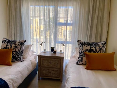 a bedroom with two beds and a window with white curtains at Central Cozy Apartment at Ane court in Swakopmund