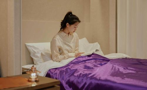 a woman sitting in bed reading a book at StayPassport Morocco Spa Incheon Songdo in Incheon