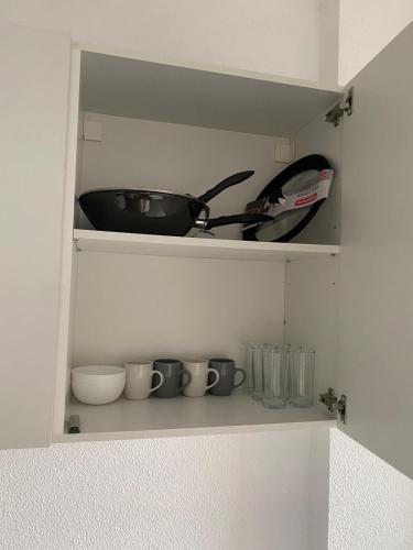 une étagère avec des tasses, une poêle et d'autres articles de cuisine dans l'établissement Appartement Cosy Elancourt, à Élancourt