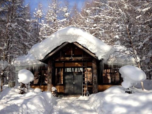 a cabin covered in snow in the woods at A traditional Japanese house with a sunken fireplace, located near Pippu Ski Resort in Pippu