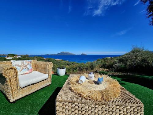 a wicker chair and table on a lawn with the ocean at SPLENDIDA VILLA SOS ARANZOS SPIAGGIA PRIVATA in Pittulongu