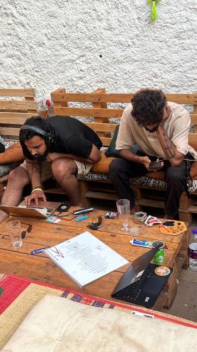 two men sitting on a wooden bench with a table at HOT - HOUSE OF TRAVELLERS, Vagator in Vagator