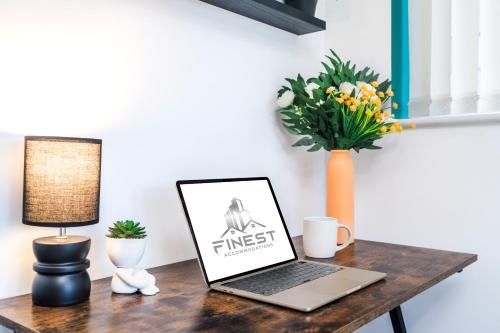 a laptop on a wooden table with a vase with flowers at Stylish Decor Close to Vibrant O2, Canary Wharf & Isle of Dogs in London