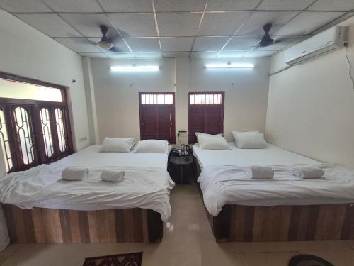 two beds in a room with white sheets and windows at Sands Courtyard in Tajpur