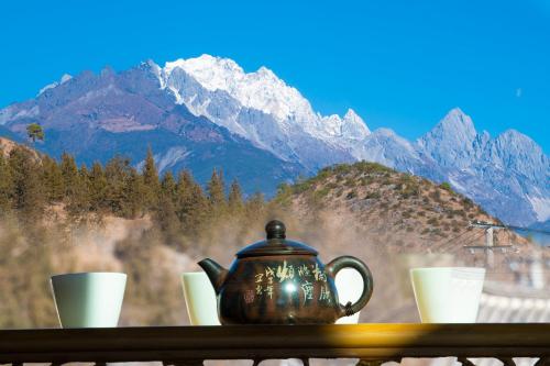 a tea kettle on a table with cups and mountains at 清舍雪山观景设计师民宿 in Lijiang