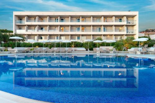 a hotel with a large swimming pool with chairs and umbrellas at Pharos Hvar Bayhill Hotel in Hvar