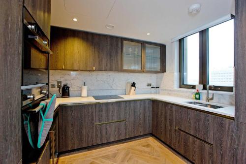a kitchen with wooden cabinets and a sink at Luxury Living with City Views with Pool and Gym AC in London