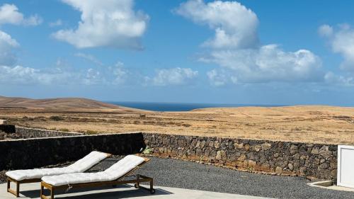 two benches sitting on a stone wall with the ocean at Casa Magafral in Tindaya with heated pool in Tindaya