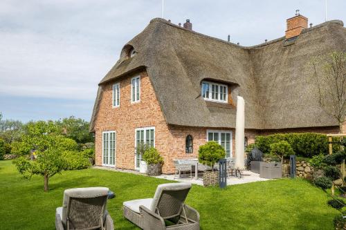 a thatch roofed house with chairs in the yard at Greta s Hüs in Archsum