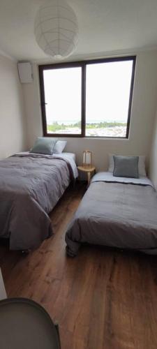two beds in a room with two large windows at Hermoso Dpto con vista Lago y Volcanes in Llanquihue