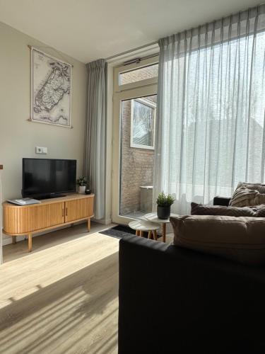 a living room with a couch and a large window at Logies het Noordwestertje in Den Burg