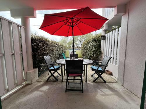 - une table et des chaises avec un parasol rouge sur la terrasse dans l'établissement Appartement 2 pièces 4 couchages Saint Pierre d'Oléron SPO000-613, à Saint-Pierre-dʼOléron