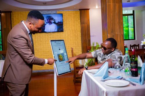 two men looking at a man holding a cell phone at Green Mountain Hotel in Arusha