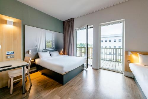 a hotel room with a bed and a desk and a balcony at B&B HOTEL Bordeaux Est 3 étoiles in Tresses