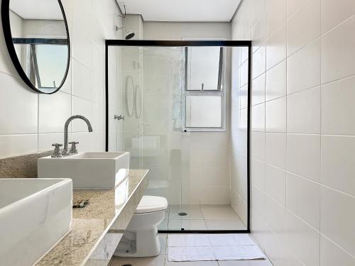 a bathroom with a toilet and a sink and a mirror at 100 metros da praia - Condomínio - 3 suítes - Churrasqueira in Guarujá
