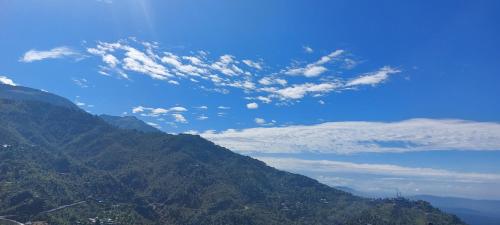 a view of a mountain with a blue sky and clouds at Mountain Heaven Mcleodganj in Dharmsala