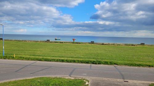 an empty road next to a field with the ocean at Driftwood, Ground floor 1 bedroom flat in Selsey