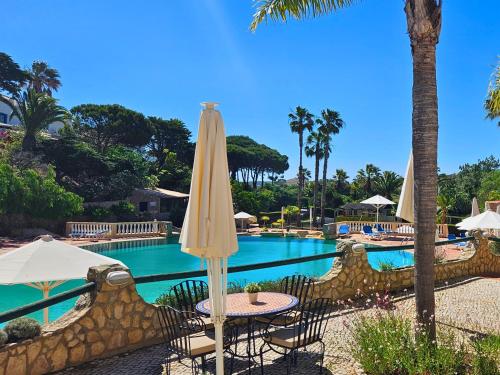 a pool with tables and umbrellas and a swimming pool at Quinta da Floresta – Santo António Villas, Golf & Spa in Budens