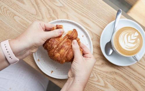 a person holding a pastry on a plate next to a cup of coffee at ARK Canary Wharf in London