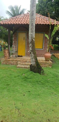 a small brick house with yellow doors and a tree at FAZENDA BOSQUE DAs PALMEIRAS in Itamaracá