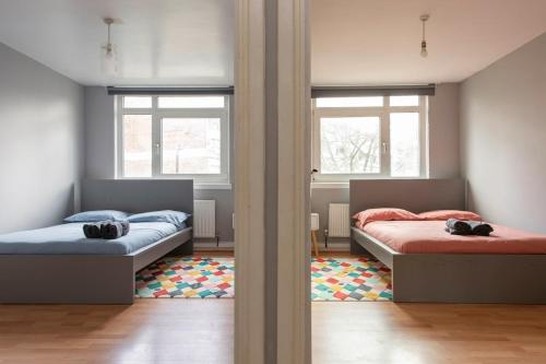 two beds in a room with two windows at Lovely 2-bed 20 mins to central London in London