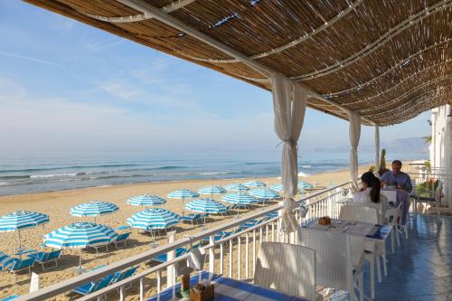 a beach with blue and white umbrellas and people sitting on the beach at Hotel Aurora in Sperlonga