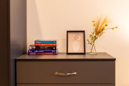 a table with books and a picture and a vase with flowers at K Suites - Rivington Apartments in Slough