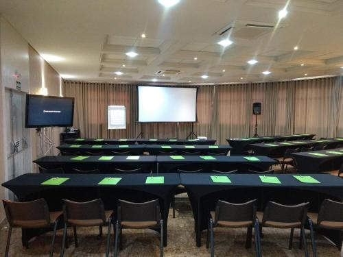 a conference room with tables and chairs and a screen at Hotel Metrópole Maringá in Maringá