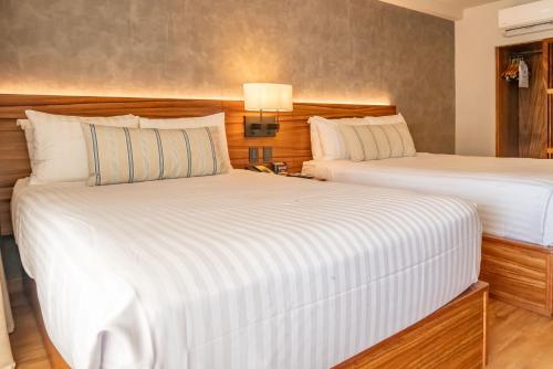 two beds in a hotel room with white sheets at Emporio Mazatlan in Mazatlán