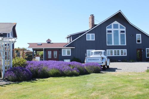 an old truck parked in front of a house with purple flowers at Dungeness Barn House Bed and Breakfast at Two Crows Farm in Sequim