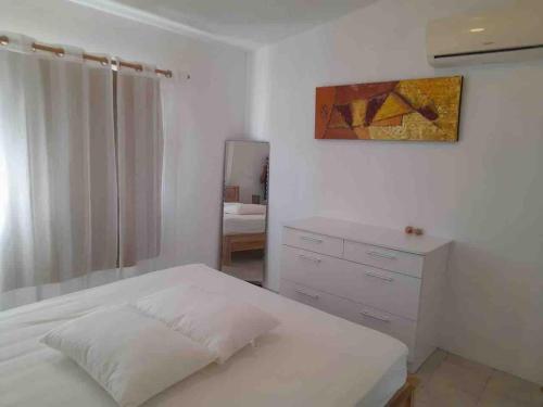 a white bedroom with a bed and a dresser at Dan Beach Apartment in Trou dʼ Eau Douce