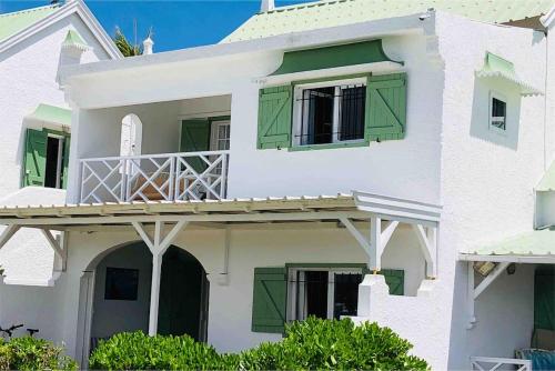 a white house with green shutters and a balcony at Dan Beach Apartment in Trou dʼ Eau Douce