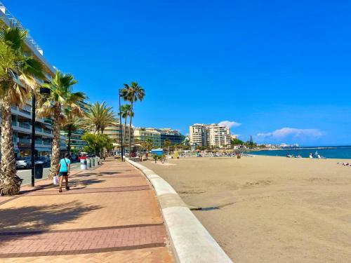 a beach with palm trees and a person walking on a sidewalk at Gå nemt til Fuengirola strand, restauranter, butikker, padel og meget mere! in Las Lagunas Mijas
