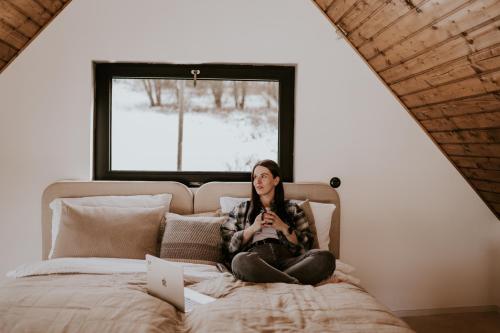 a woman sitting on a bed in front of a window at Kamienna Azyl - domek z sauną i balią w Sudetach in Kamienna