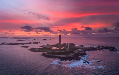 a lighthouse on the shore of the ocean with a sunset at GWEL KAER - Maison tout confort petite vue mer in Plouarzel