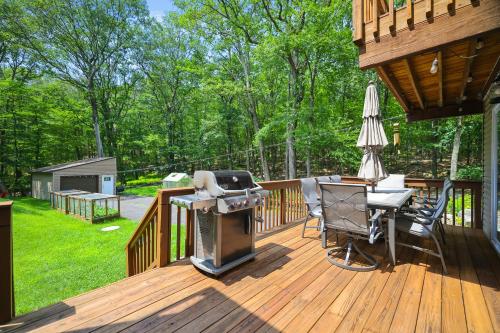 a wooden deck with a grill and chairs on it at Secluded Cabin, Jacuzzi, Pool Table, King Bed & Fire Pit in Bushkill